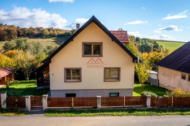 A family house in Medzev with a pyramidal roof, a fenced yard with a lawn, autumn landscape.