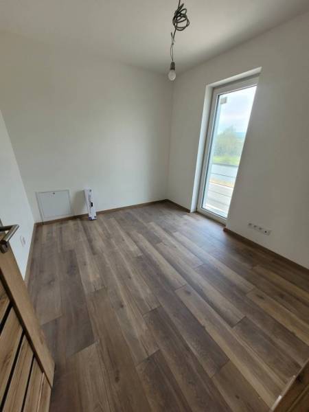 A room in a family house with a wooden-patterned floor and a large window.