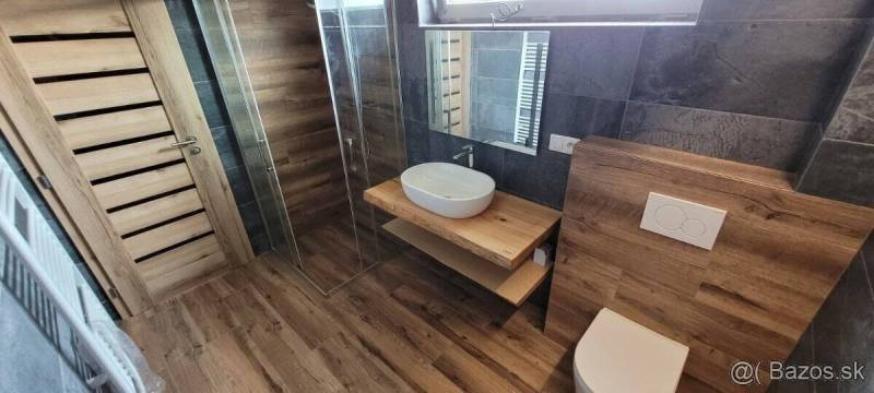 A bathroom in a family house with a sink, a shower corner, and a floor with a wooden decor.