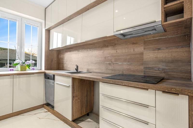 A kitchen in a 3-room apartment with light cabinets and wooden elements, with a large window.