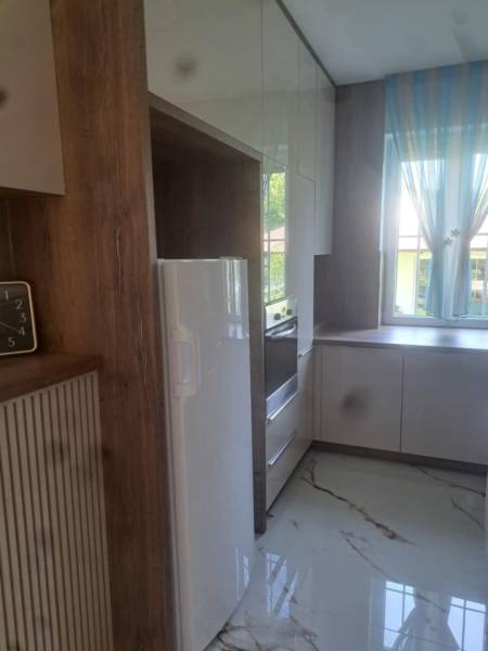 A kitchen in a 3-room apartment with tiles, a white appliance, and a large window.