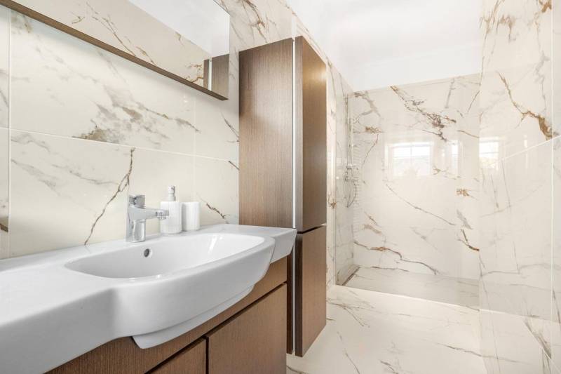 Bathroom with a shower and a sink in a 3-room apartment, light tiles with a marble pattern.