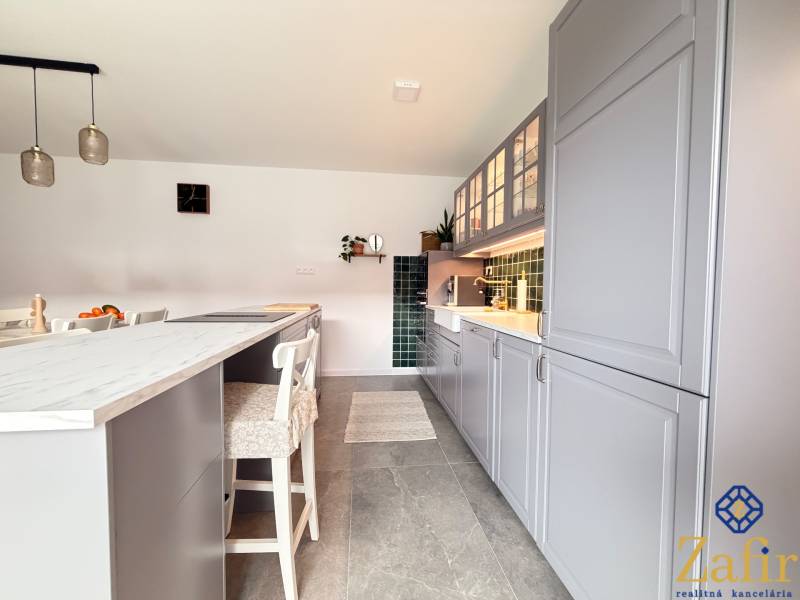 A kitchen in a family house with an island, gray cabinets, and green tiles.