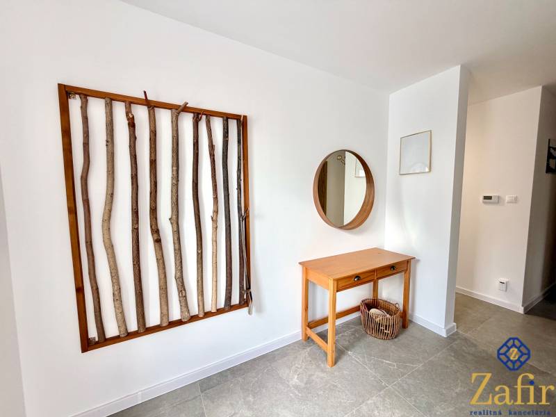 In the interior of a family house, a wall is decorated with a frame with branches, a table, and a mirror.