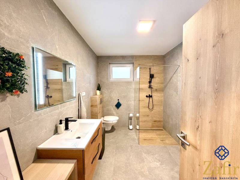 A bathroom in a family house with a simple design, gray walls, and wooden decorations.