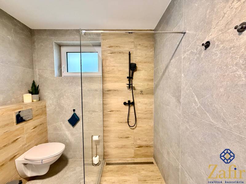 Family house bathroom with a toilet, shower corner, and wooden decor flooring.