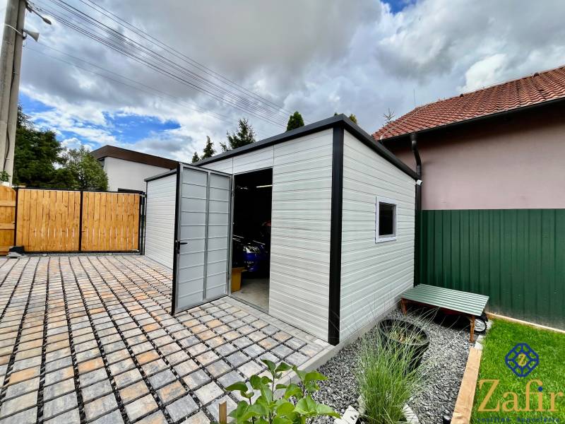 A family house in Trnava with an outbuilding and a wrought iron gate on a paved courtyard.