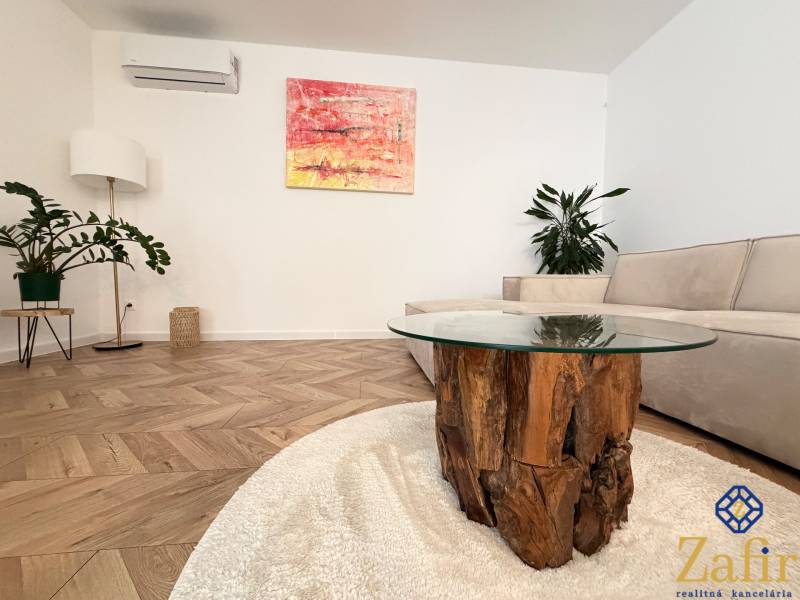 Living room with a sofa, wooden and glass table, plants, and a floor with a wooden decor.