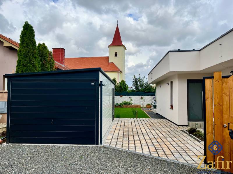 A family house in Trnava with a garden, garage, and a church in the background.