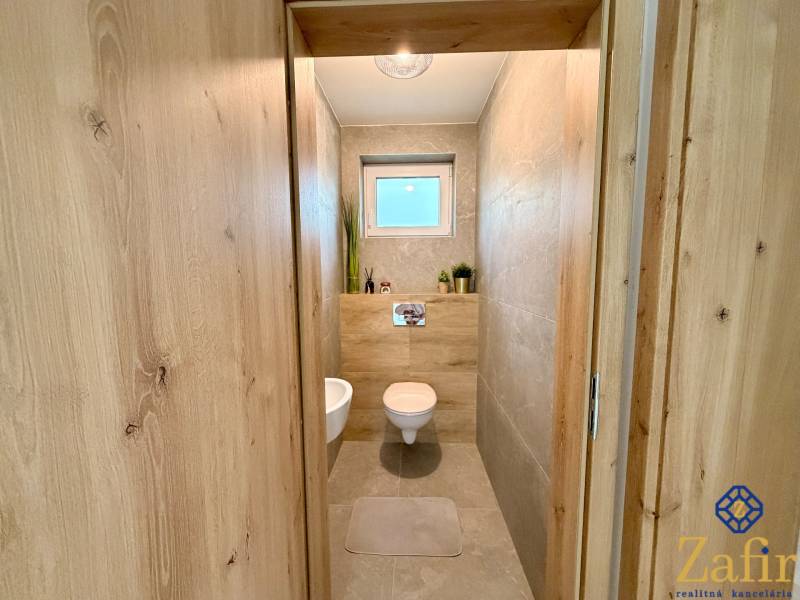 Bathroom with wood-patterned flooring, ceramic tiles, and a toilet in a family house.