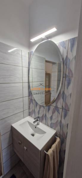 Compact bathroom in a 2-room apartment with an oval mirror and a floor with a wooden decor.