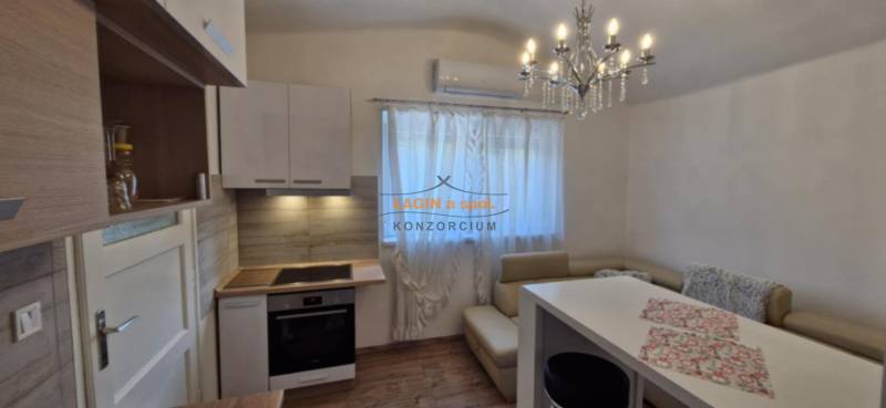 A kitchen in a 2-room apartment with a chandelier, a dining table, and a floor with a wooden design.
