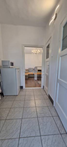 A corridor with tiles leading into a room with a wooden decor floor in a 2-room apartment.