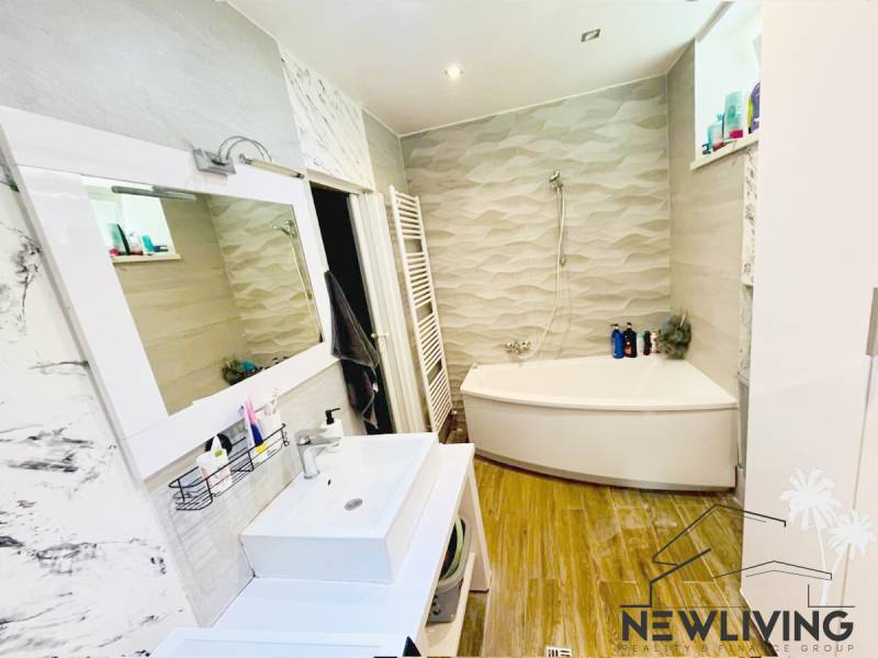 A bathroom in a 3-room apartment with a corner bathtub and a floor with a wood design.