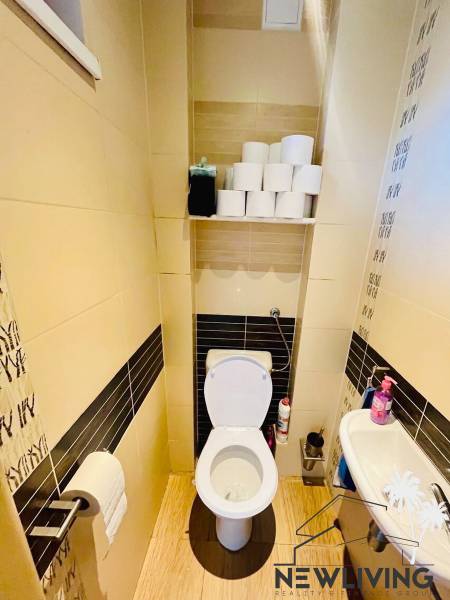 A toilet with a shelf, a sink, and a floor with a wooden decor in a 3-room apartment.