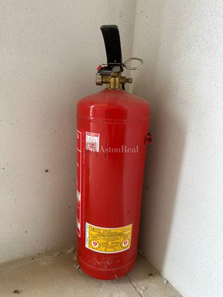 Fire extinguisher in the corner of the Garage space on the concrete floor.
