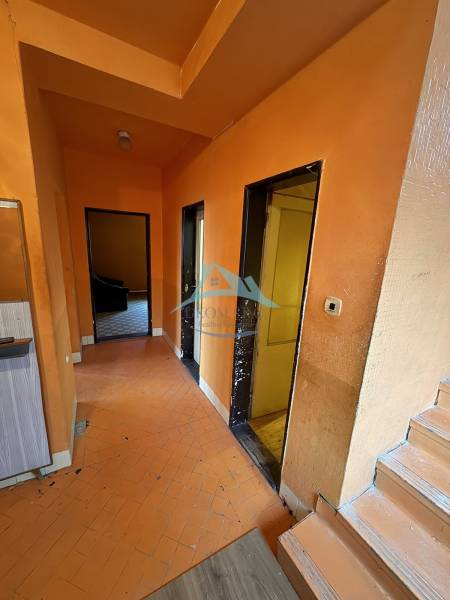 A hallway in a family house with orange walls and a wooden-patterned floor.