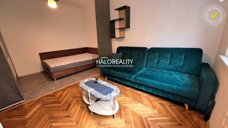 A room in a one-bedroom apartment with a sofa, bed, and wooden decor flooring.