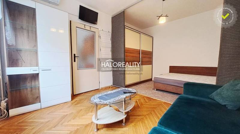 A room with a wooden decor floor, a sofa, a table, and a built-in wardrobe in a studio apartment.