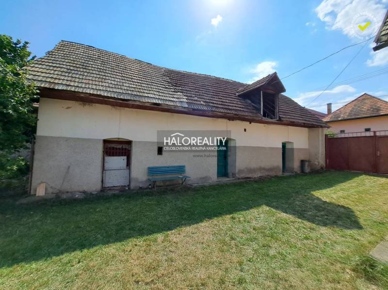 A family house in Zvolen with a wooden roof, a green yard, a bench, and a concrete facade.