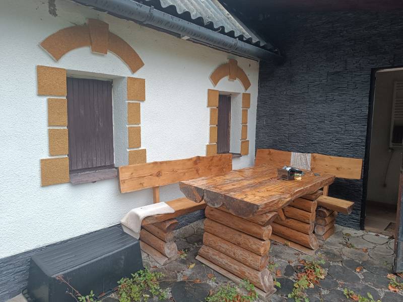 A cottage in Píla with wooden seating on a stone terrace and decorated windows.