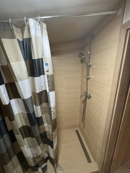 A shower corner in a cabin with tiles and a curtain in a striped design.