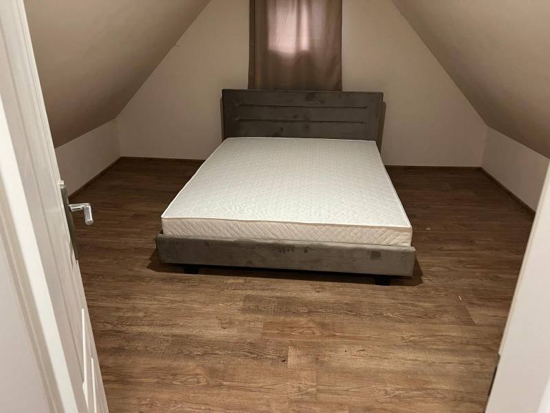 Attic room in a cottage with a bed and a wooden decor floor.