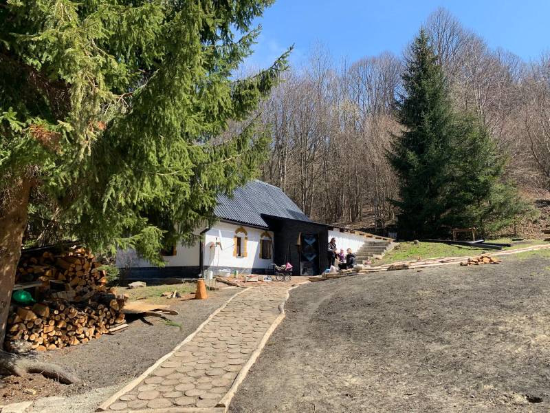 A cottage surrounded by forest in the village of Píla with a footpath and stored wood.
