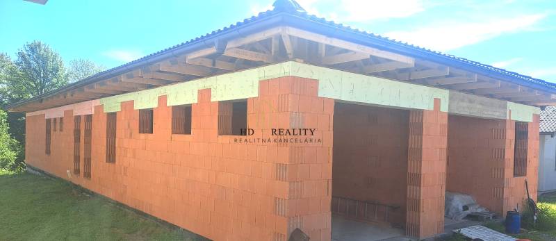 A family house under construction in Hokovce with unplastered brick walls and a wooden roof structure.