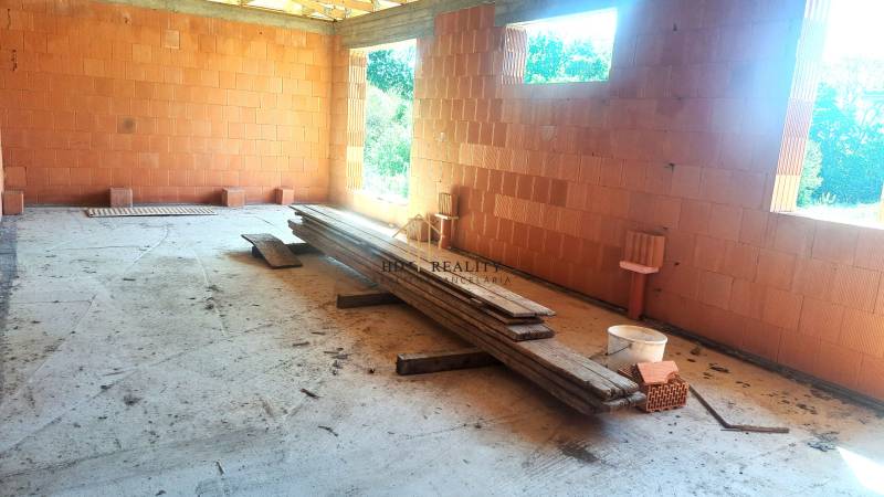 Construction of a family house in Hokovce with raw brick walls and wooden boards on the ground.