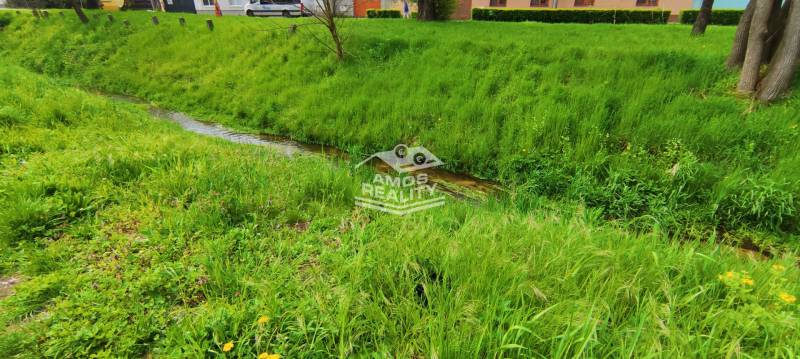 In the picture, a stream flows surrounded by lush grass, near Štúrova Street.