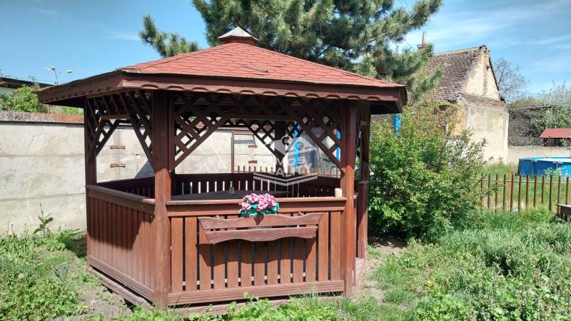 A wooden gazebo surrounded by greenery and a fence on Štúrova Street near a family house.