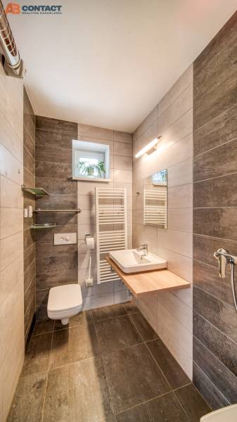 A bathroom in a family house with dark tiles and a wooden decor floor.
