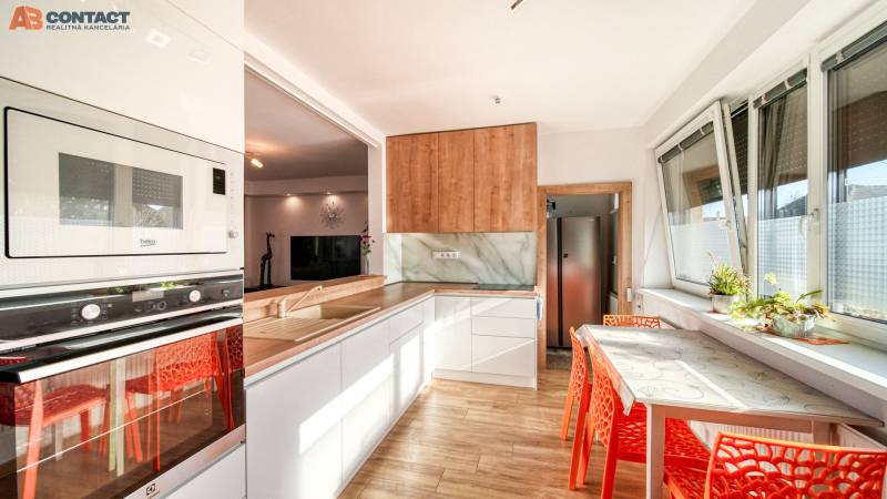 A kitchen in a family house with a sink, refrigerator, oven, table, and orange chairs.