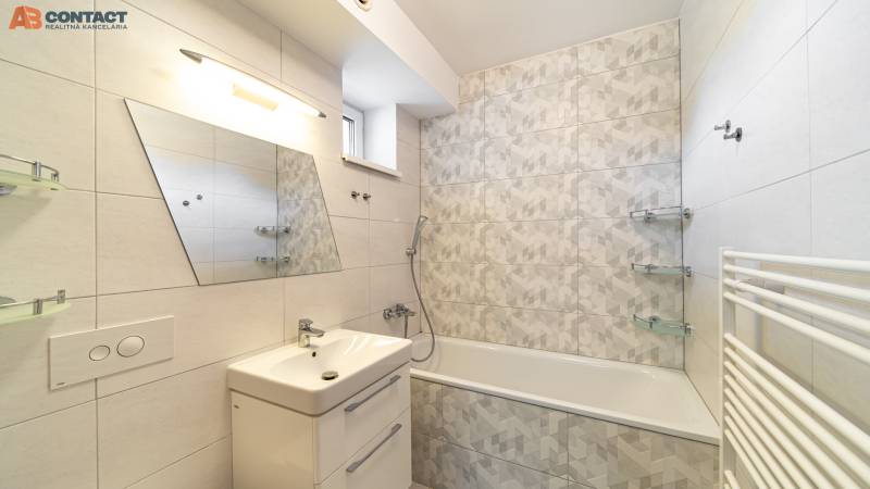 A bathroom in a family house with a rectangular bathtub and an asymmetrical mirror on the wall.