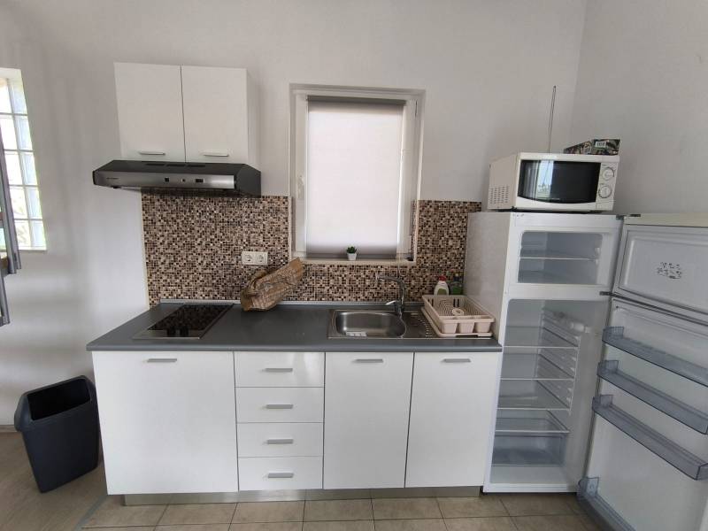 A kitchen in a 3-room apartment with a cooktop, sink, and a free-standing refrigerator.