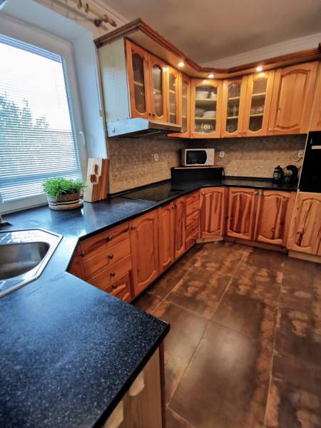 A kitchen in a family house with wooden cabinets, a dark countertop, and tiles.