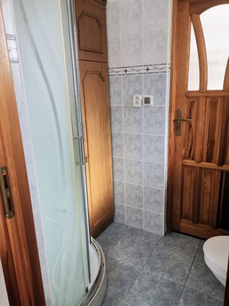 Bathroom in a family house with a tray shower, light tiles, and wooden details.