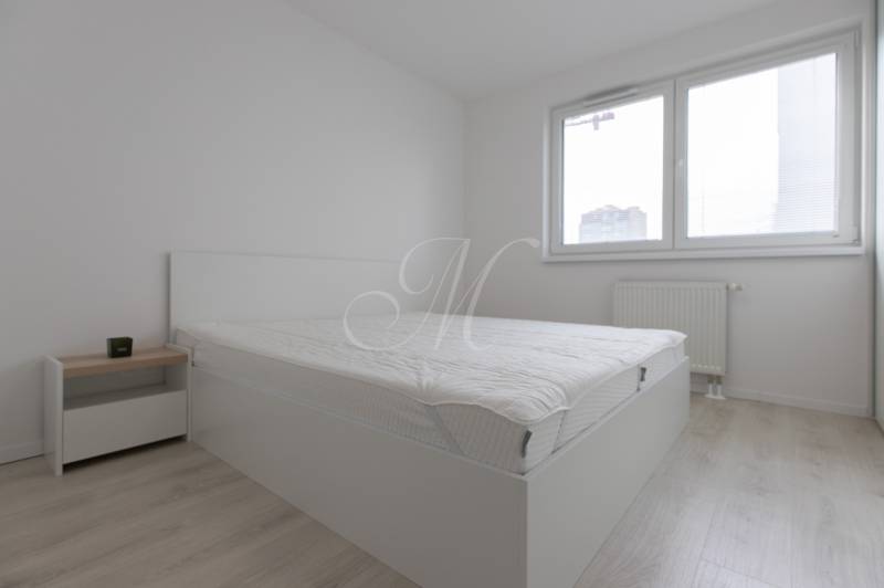 A bright bedroom with a bed and wood-decor flooring in a 2-room apartment.