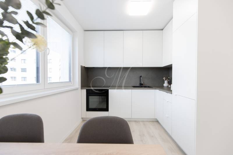 A kitchen in a 2-room apartment with white cabinets, a gray countertop, and a large window.