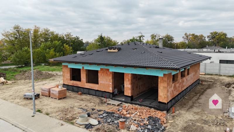 A family house under construction in Bernolákovo, surrounded by greenery and building materials.