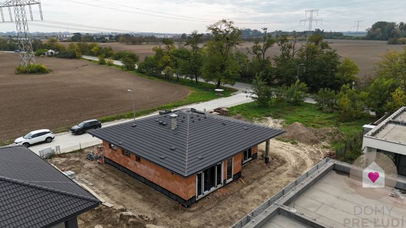 A family house in Bernolákovo with a black roof and surrounding fields under construction.