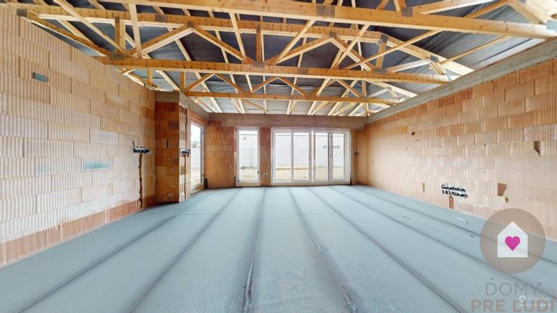 The interior of a house under construction with exposed brick walls and roof structure.