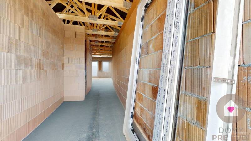 An unfinished interior of a family house with brick walls and wooden roof beams.