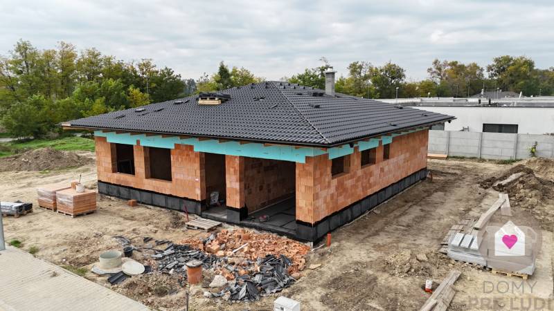 A family house in Bernolákovo under construction, surrounding trees, gray roof.