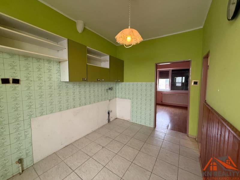 A kitchen in a family house with tiles, green walls, and wall cabinets.