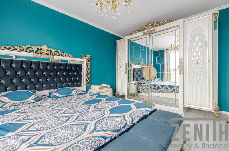 A bedroom in a family house with a turquoise wall, a mirrored wardrobe, and a decorative chandelier.