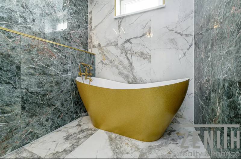 Golden bathtub with marble walls in the bathroom of a family house.