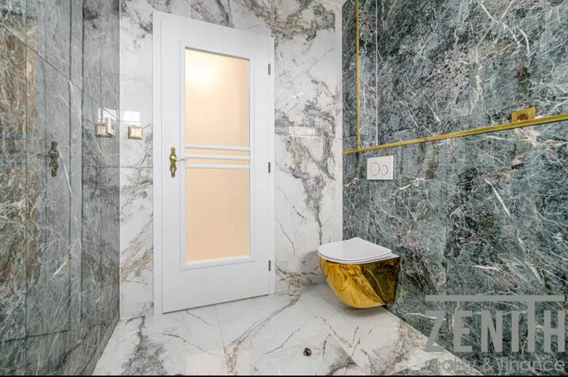 Bathroom with marble tiles and a golden toilet in a family house.