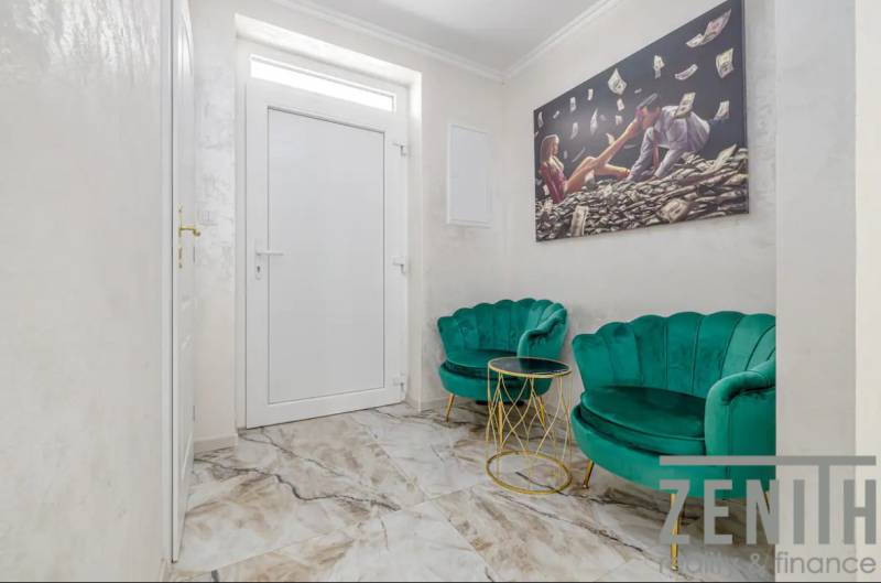 Interior of a family house with white walls, emerald armchairs, and a painting on the wall.